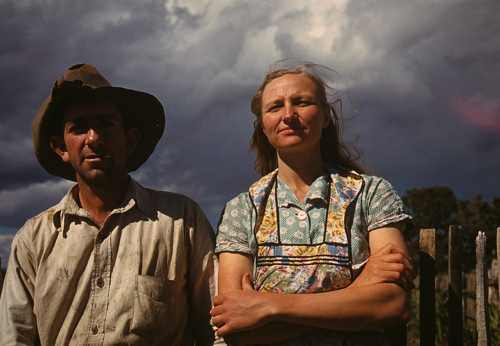 A farm couple in front of a fence and storm clouds, colors clean and deep after restoration